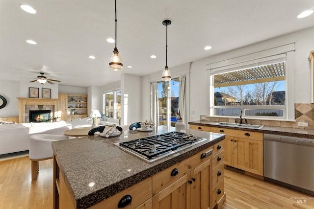 kitchen with decorative light fixtures, a kitchen island, sink, light wood-type flooring, and stainless steel appliances