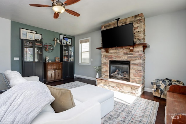 living area featuring a stone fireplace, ceiling fan, wood finished floors, and baseboards