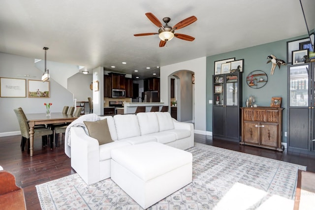 living area featuring arched walkways, a ceiling fan, dark wood-style floors, baseboards, and recessed lighting