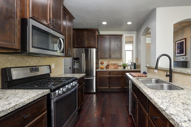 kitchen with stainless steel appliances, a sink, light stone countertops, dark wood finished floors, and recessed lighting