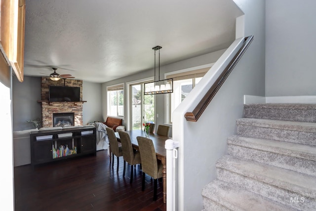 stairs with wood-type flooring, ceiling fan, and a stone fireplace