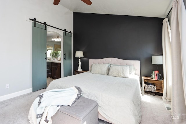 carpeted bedroom with a barn door, baseboards, a ceiling fan, and ensuite bath