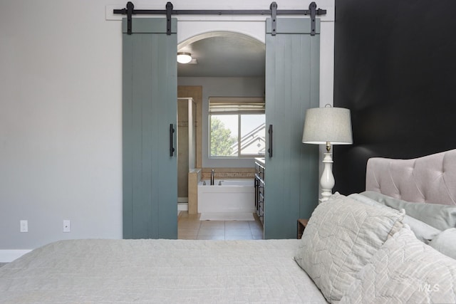 bedroom featuring a barn door, tile patterned floors, arched walkways, and ensuite bathroom