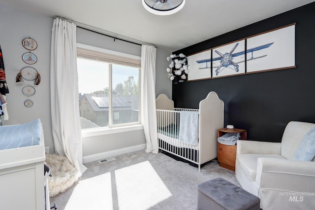 carpeted bedroom featuring a nursery area and baseboards