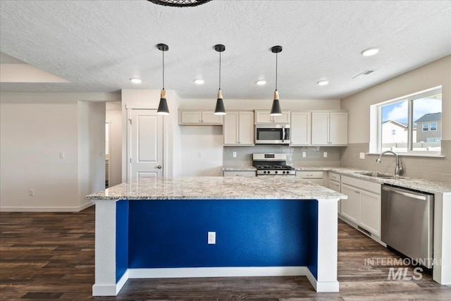 kitchen featuring sink, light stone counters, hanging light fixtures, a kitchen island, and stainless steel appliances