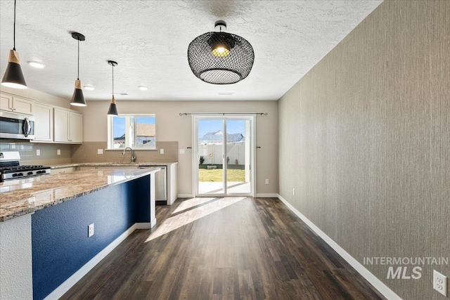 kitchen featuring sink, light stone counters, decorative light fixtures, dark hardwood / wood-style flooring, and stainless steel appliances