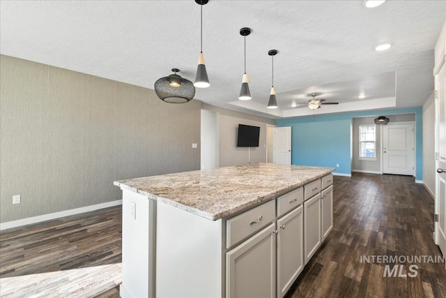 kitchen featuring dark hardwood / wood-style flooring, hanging light fixtures, a center island, light stone counters, and a raised ceiling