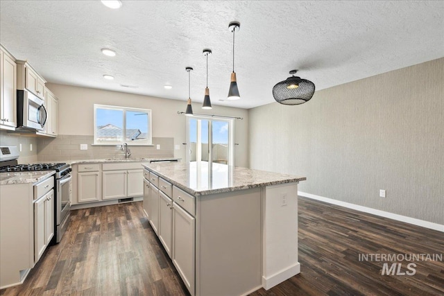 kitchen with sink, appliances with stainless steel finishes, hanging light fixtures, light stone counters, and a kitchen island