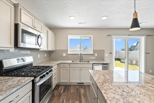 kitchen with sink, light stone counters, decorative light fixtures, appliances with stainless steel finishes, and dark hardwood / wood-style flooring