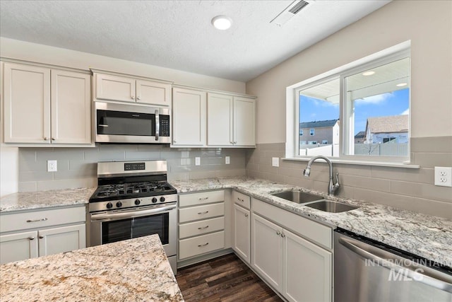 kitchen with appliances with stainless steel finishes, white cabinetry, sink, light stone countertops, and dark wood-type flooring