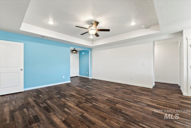 empty room featuring dark hardwood / wood-style flooring, a textured ceiling, a raised ceiling, and ceiling fan