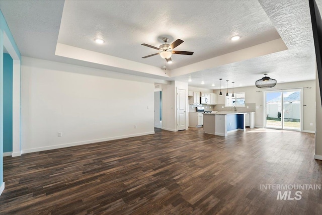 unfurnished living room featuring dark wood-type flooring, a raised ceiling, and a textured ceiling