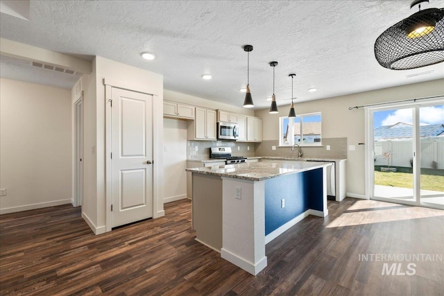 kitchen featuring pendant lighting, dark wood-type flooring, appliances with stainless steel finishes, tasteful backsplash, and a kitchen island