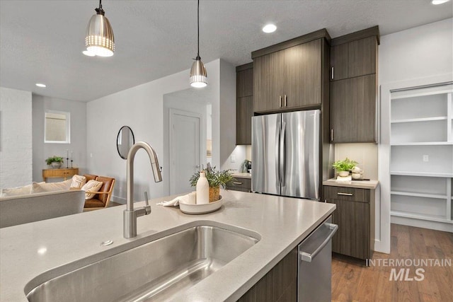 kitchen with dark brown cabinets, decorative light fixtures, light countertops, appliances with stainless steel finishes, and a sink