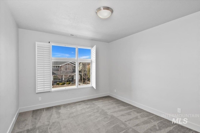 carpeted spare room featuring a textured ceiling and baseboards