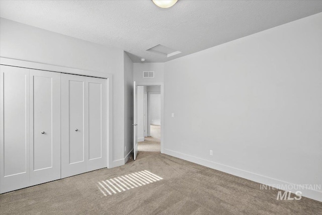 unfurnished bedroom with visible vents, attic access, carpet floors, a closet, and a textured ceiling