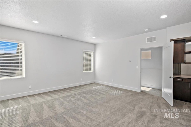 spare room featuring light carpet, visible vents, a textured ceiling, and baseboards