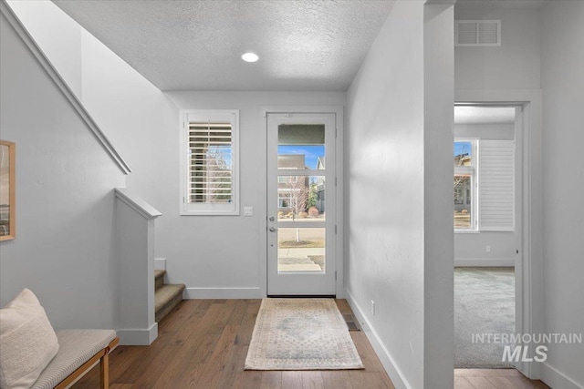 doorway to outside featuring visible vents, a textured ceiling, stairway, wood-type flooring, and baseboards