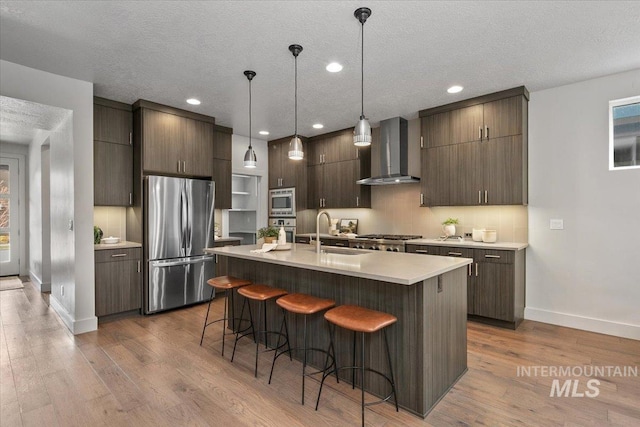 kitchen featuring a sink, a kitchen breakfast bar, appliances with stainless steel finishes, wall chimney exhaust hood, and light countertops