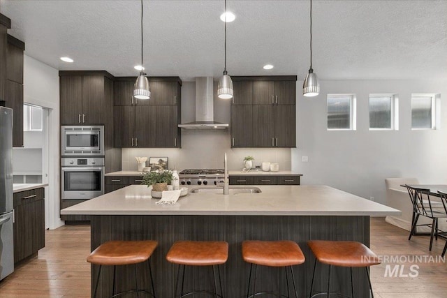 kitchen with a sink, appliances with stainless steel finishes, a breakfast bar, and wall chimney range hood