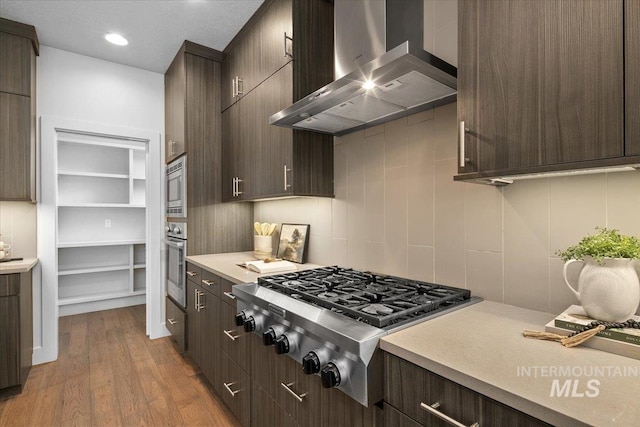 kitchen featuring dark brown cabinetry, wall chimney exhaust hood, light countertops, and appliances with stainless steel finishes