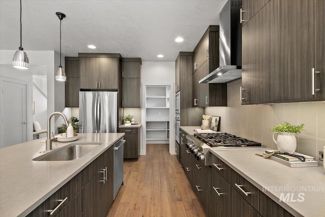 kitchen featuring light wood finished floors, a sink, appliances with stainless steel finishes, wall chimney range hood, and modern cabinets