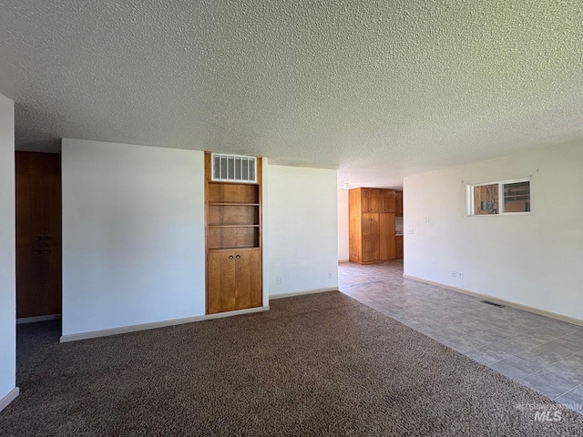 spare room with visible vents, carpet flooring, a textured ceiling, and baseboards