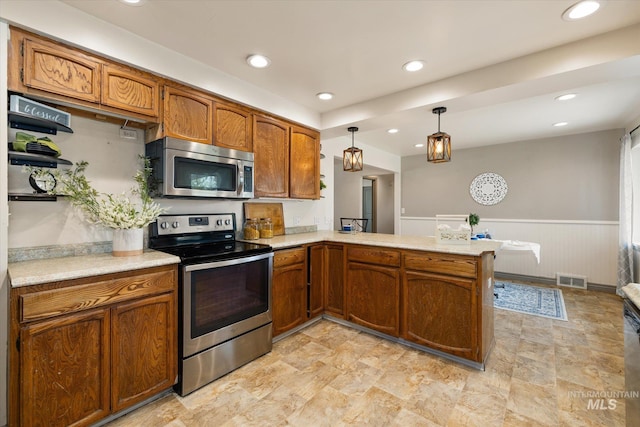 kitchen featuring light countertops, stainless steel appliances, brown cabinetry, and wainscoting