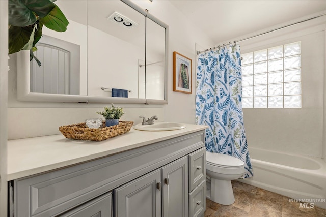 full bathroom featuring vanity, shower / tub combo with curtain, stone finish flooring, and toilet