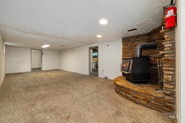 finished basement with carpet floors, a wood stove, and visible vents