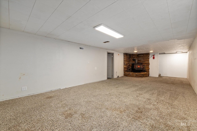 finished below grade area with carpet flooring, visible vents, and a wood stove