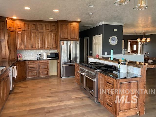 kitchen with crown molding, hanging light fixtures, premium appliances, decorative backsplash, and light wood-type flooring