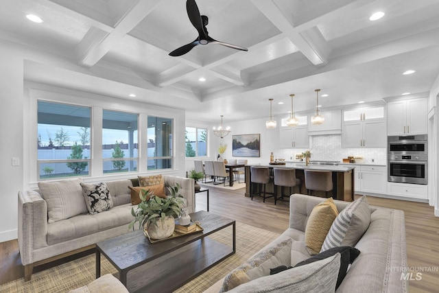 living room with wood-type flooring, coffered ceiling, ceiling fan with notable chandelier, and beam ceiling