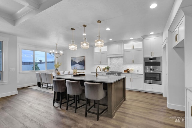 kitchen with stainless steel double oven, decorative light fixtures, a center island with sink, and white cabinets