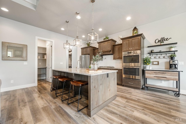 1071 W Rose Quartz St, Kuna, ID 83634 - kitchen featuring appliances with stainless steel finishes, a kitchen island with sink, light wood-style flooring, a breakfast bar area, and light stone counters