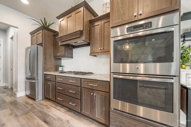 1071 W Rose Quartz St, Kuna, ID 83634 - kitchen featuring stainless steel appliances, light wood-style floors, backsplash, light stone counters, and baseboards