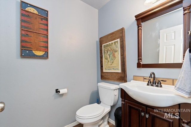 half bathroom featuring vanity, toilet, and baseboards