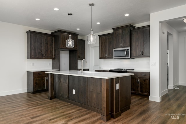 kitchen featuring dark brown cabinets, pendant lighting, a kitchen island with sink, dark wood-type flooring, and tasteful backsplash