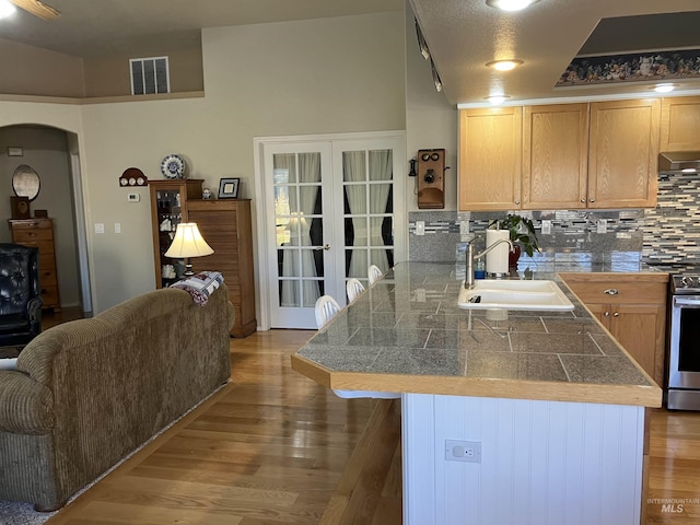 kitchen with visible vents, tile counters, stainless steel stove, under cabinet range hood, and a sink