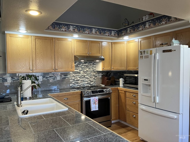 kitchen with tile counters, a sink, stainless steel appliances, under cabinet range hood, and backsplash