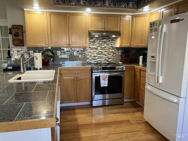 kitchen featuring white refrigerator with ice dispenser, tile counters, stainless steel electric range oven, under cabinet range hood, and a sink