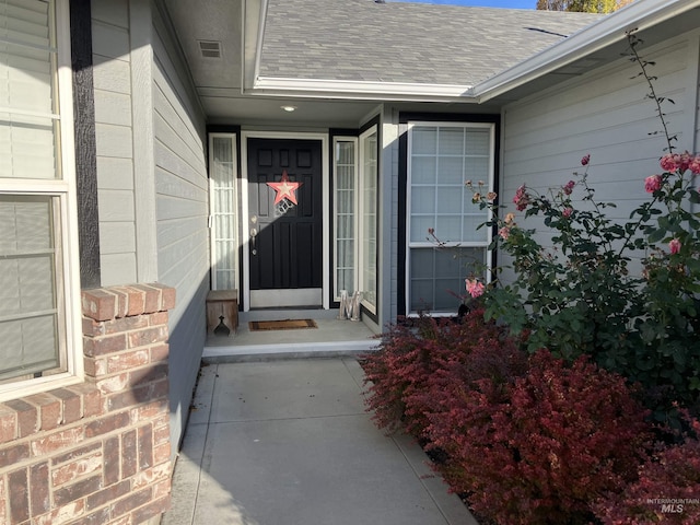 property entrance featuring a shingled roof, visible vents, and brick siding