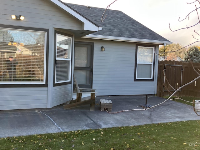 view of home's exterior featuring a shingled roof, fence, and a patio