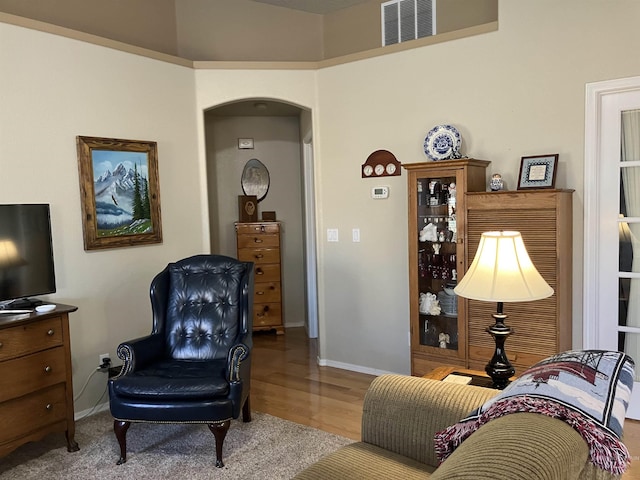 living area with baseboards, visible vents, arched walkways, and light wood-style flooring