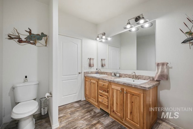 full bath featuring wood finished floors, double vanity, and toilet
