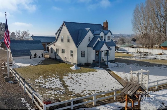 snow covered back of property featuring a chimney and fence