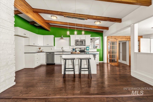 kitchen with white cabinets, dark countertops, appliances with stainless steel finishes, lofted ceiling with beams, and a sink