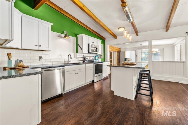 kitchen with dark wood-style flooring, lofted ceiling with beams, appliances with stainless steel finishes, a sink, and decorative backsplash