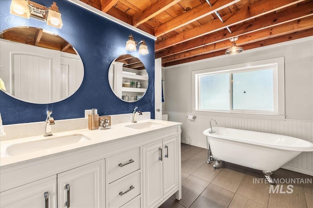 bathroom featuring a sink, wood ceiling, beam ceiling, and a wainscoted wall