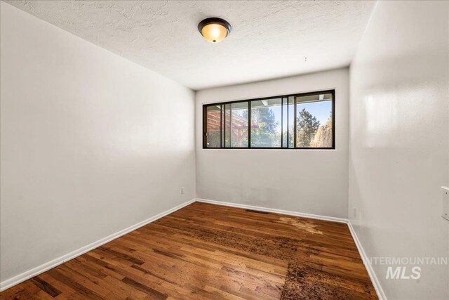 spare room featuring a textured ceiling, baseboards, visible vents, and wood finished floors